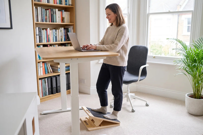Person standing on the Reoviva Slant Board at a home-office desk during a call