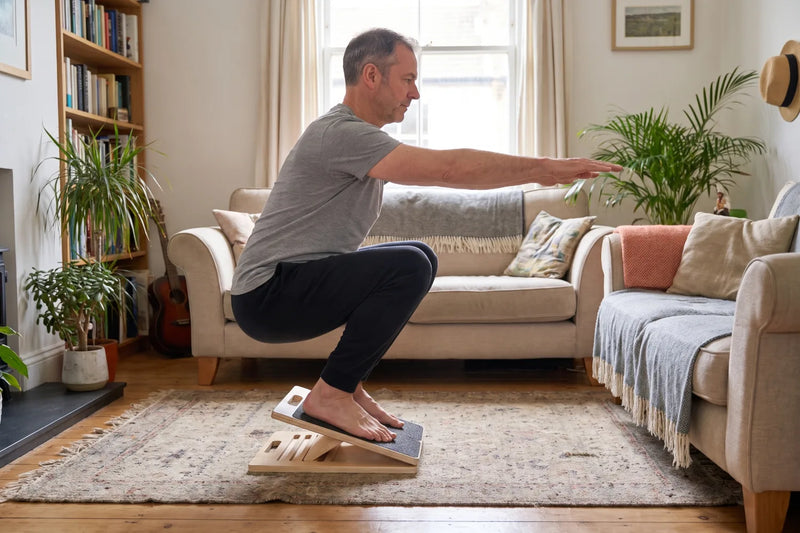 Man in his fifties doing a heels-up squat on the flipped Reoviva Slant Board in the living room